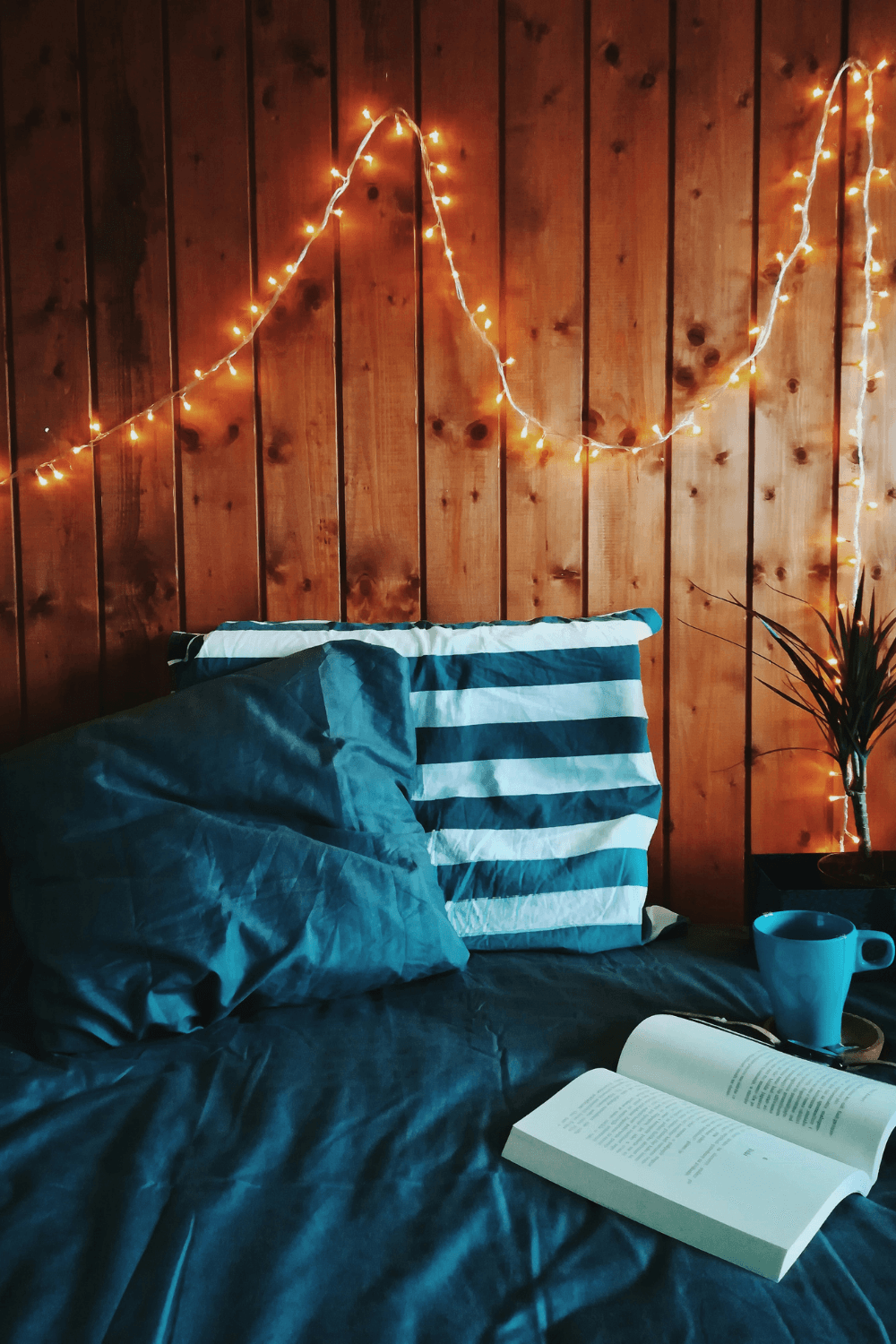 Bed with blue duvet and book with fairy lights in the background