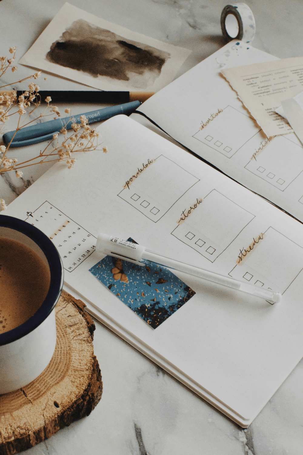 Bullet journal open on table next to pens and coffee mug