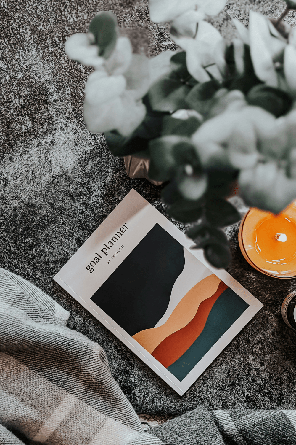 Goal planner on grey rug next to blanket and candle