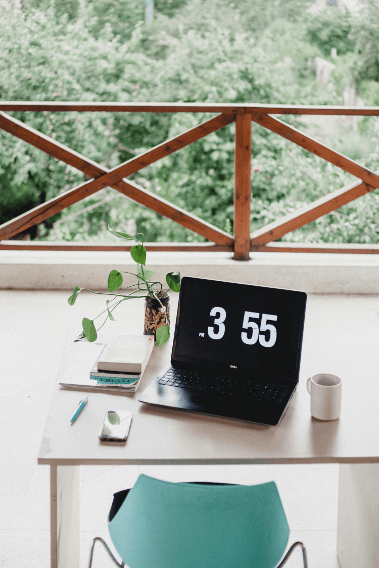 Laptop showing the time next to mug and plant