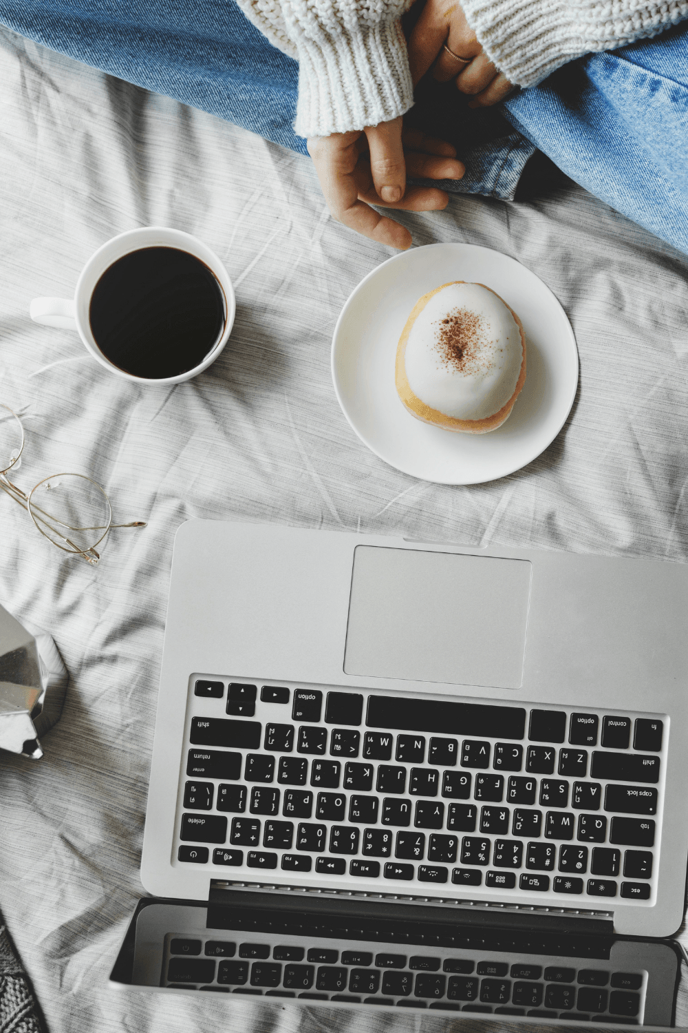 Open laptop on duvet with tea and doughnut