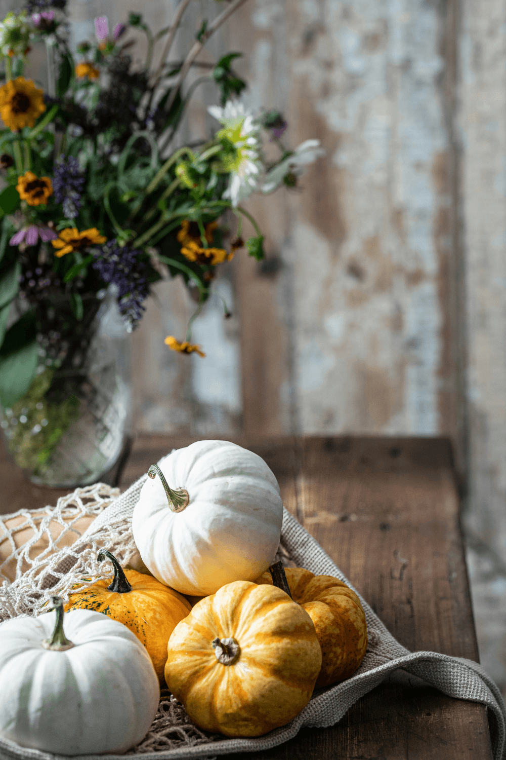 Pumpkins sitting on a table next to a vase of flowers
