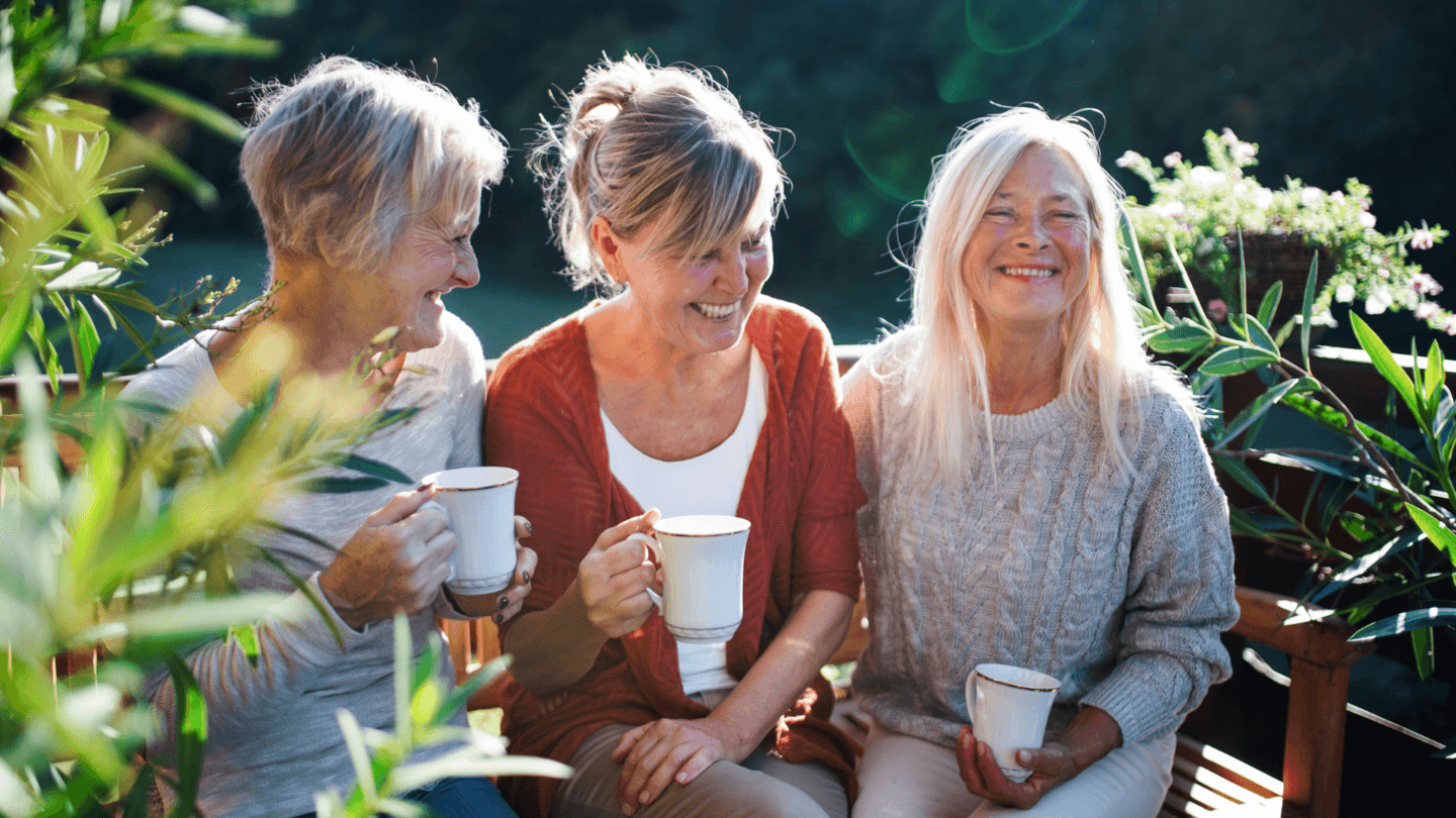 Three older women sitting together with mugs in hand