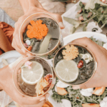 Three people holding drinks with fruit and flowers floating on top