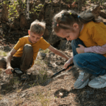 Two children looking at the ground with magnifying glasses