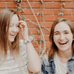 Two smiling girls standing in front of a red brick wall