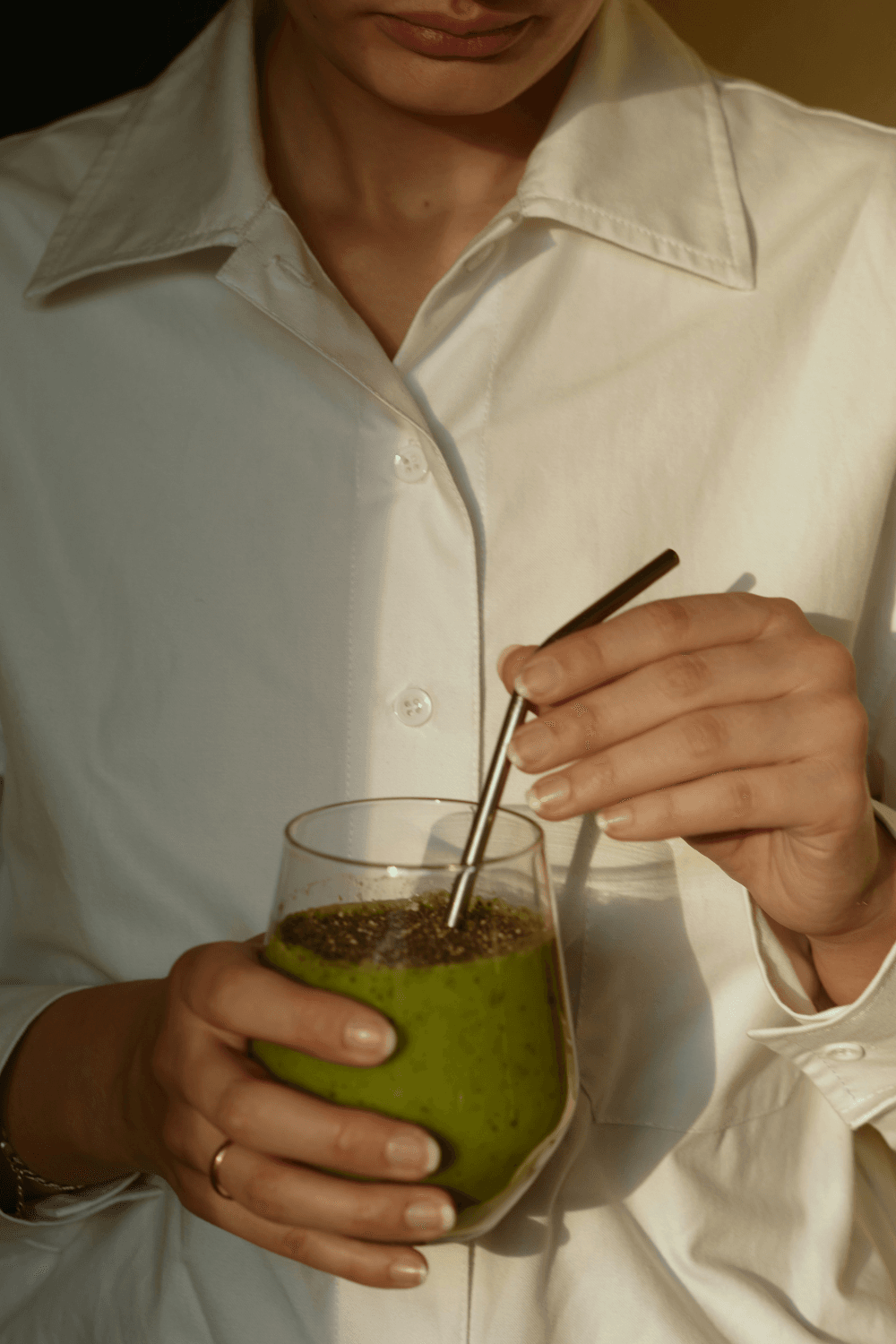 Woman holding a green smoothie and metal straw