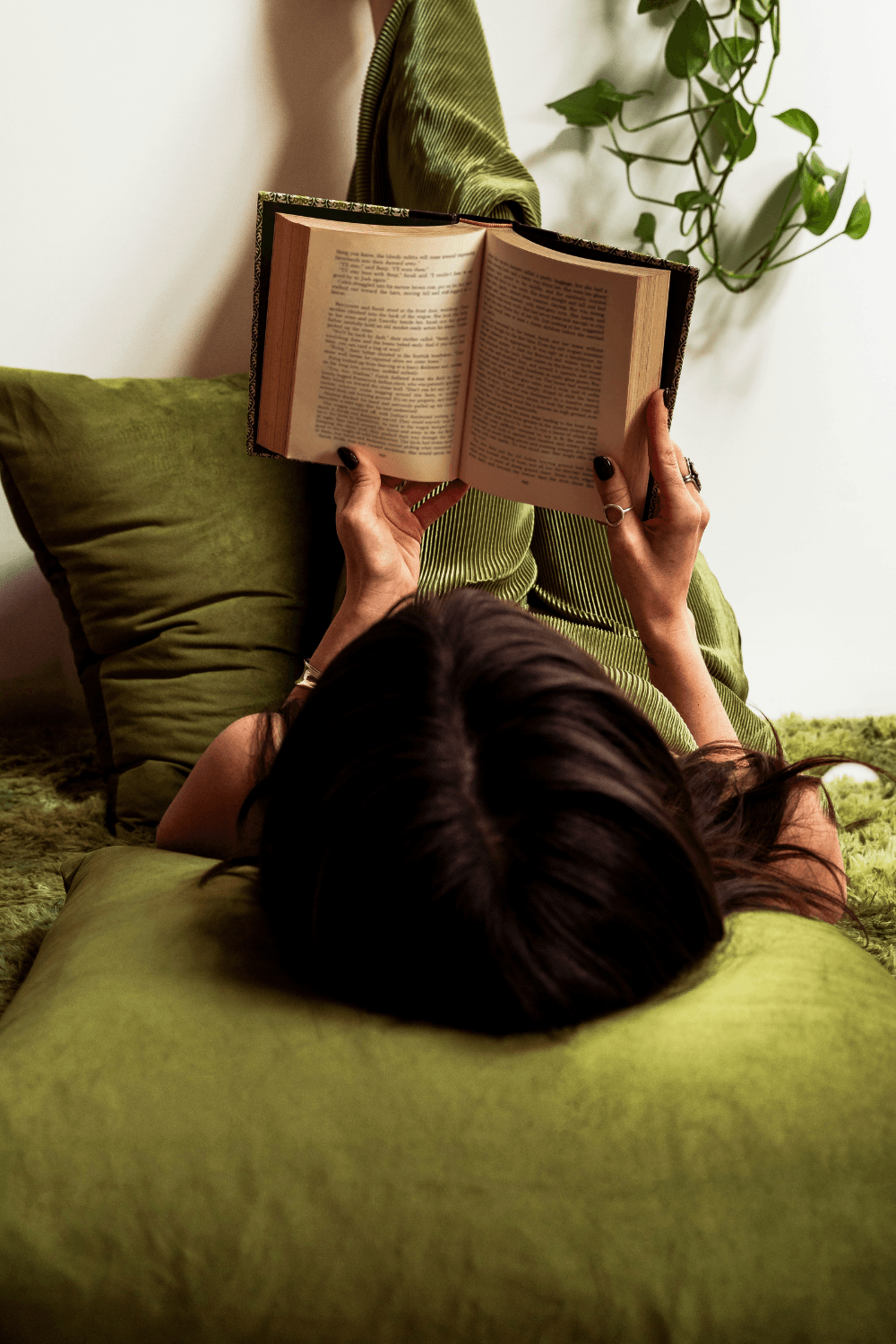 Woman lying on green sofa reading a book