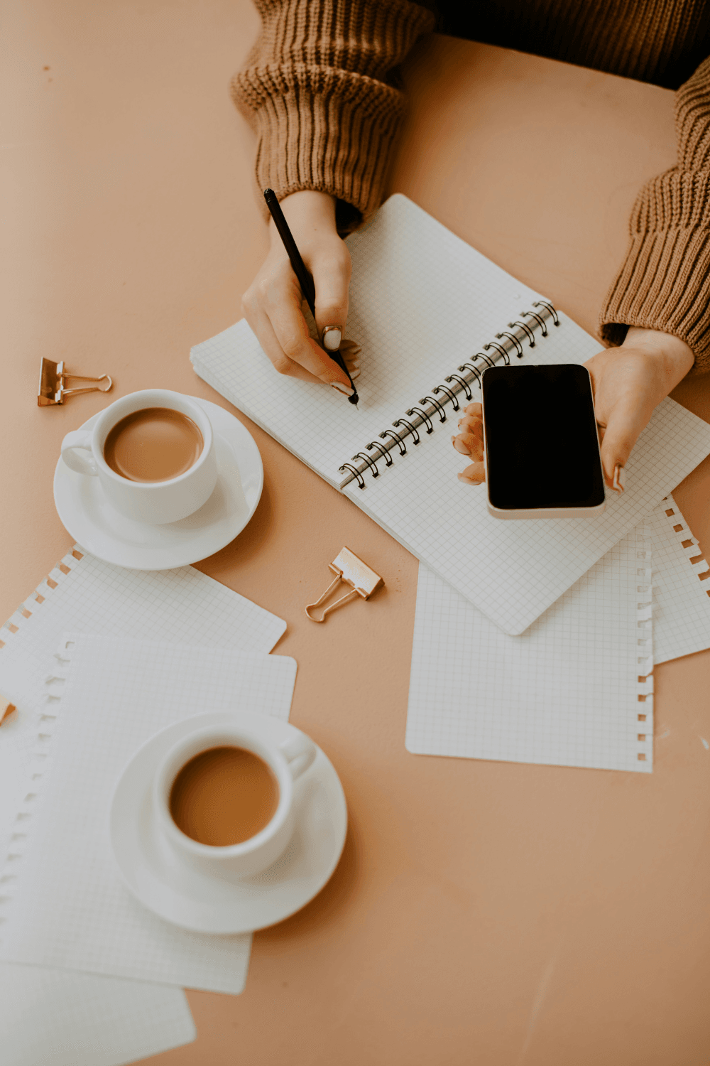 Woman making notes on desk with mobile phone in hand
