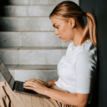 Woman sitting on dark stairwell working on laptop