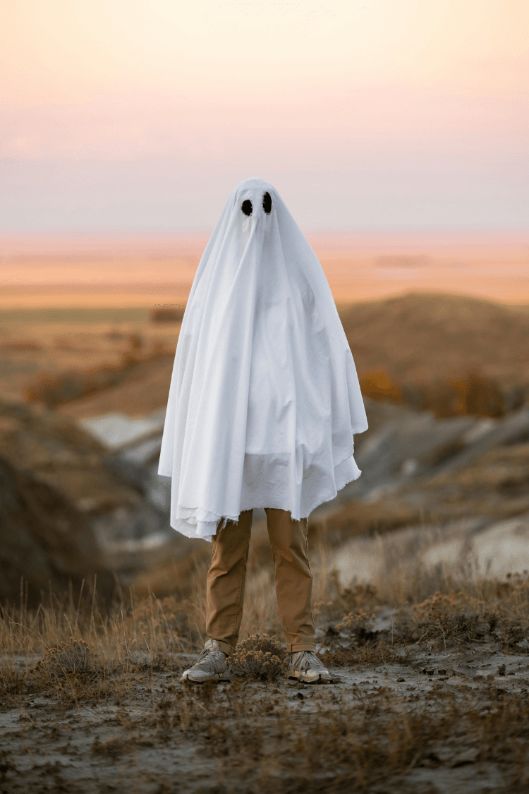 Child standing in a field wearing a white sheet to look like a ghost