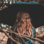Girl in denim jacket holding umbrella above her head in forest