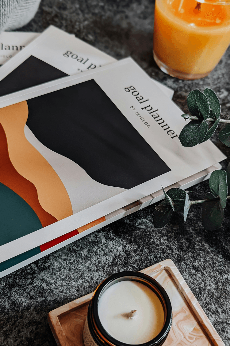 Goal planner book next to candle and glass of orange juice