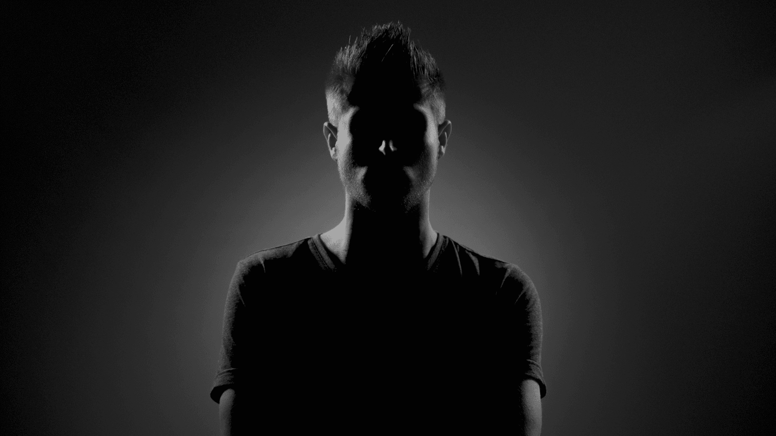 Man wearing dark clothing in dark room with face unclear
