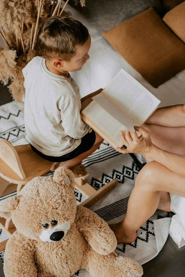 Mother reading book to child with teddy bear in corner