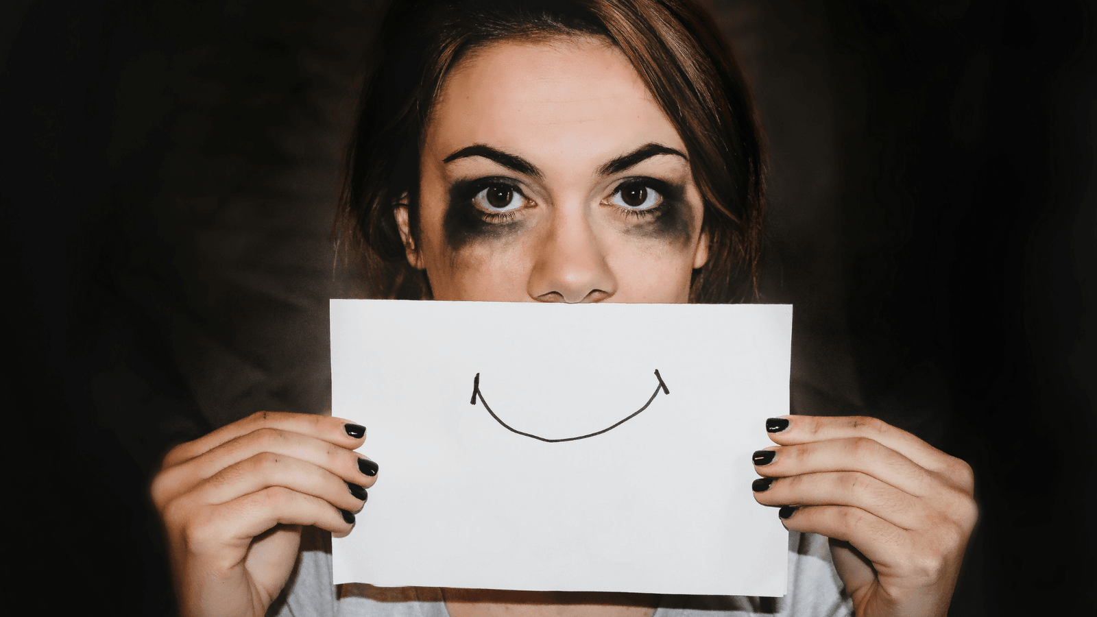 Sad woman holding paper with a smile on it over her mouth