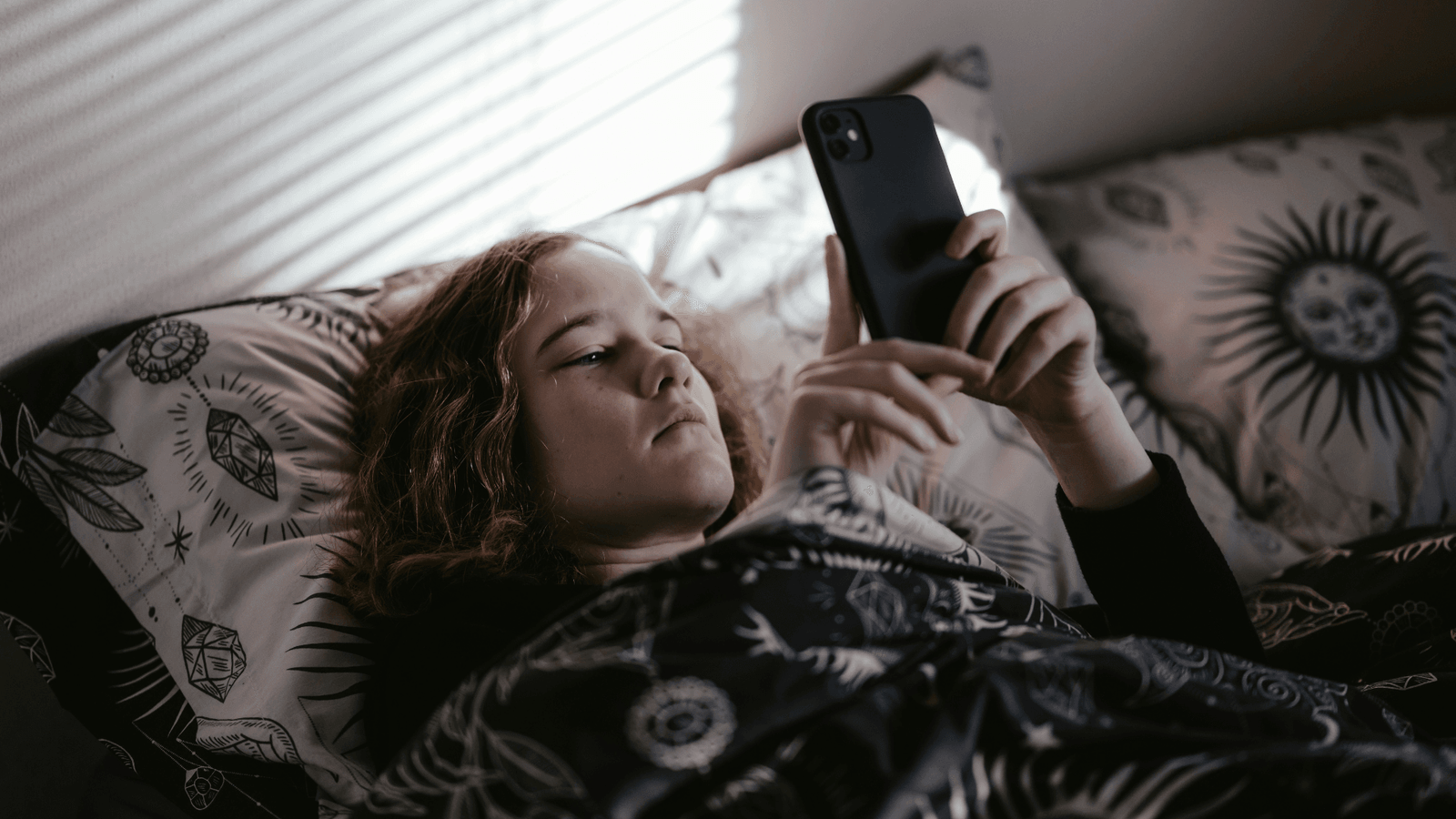 Teenager lying on her bed looking at her phone