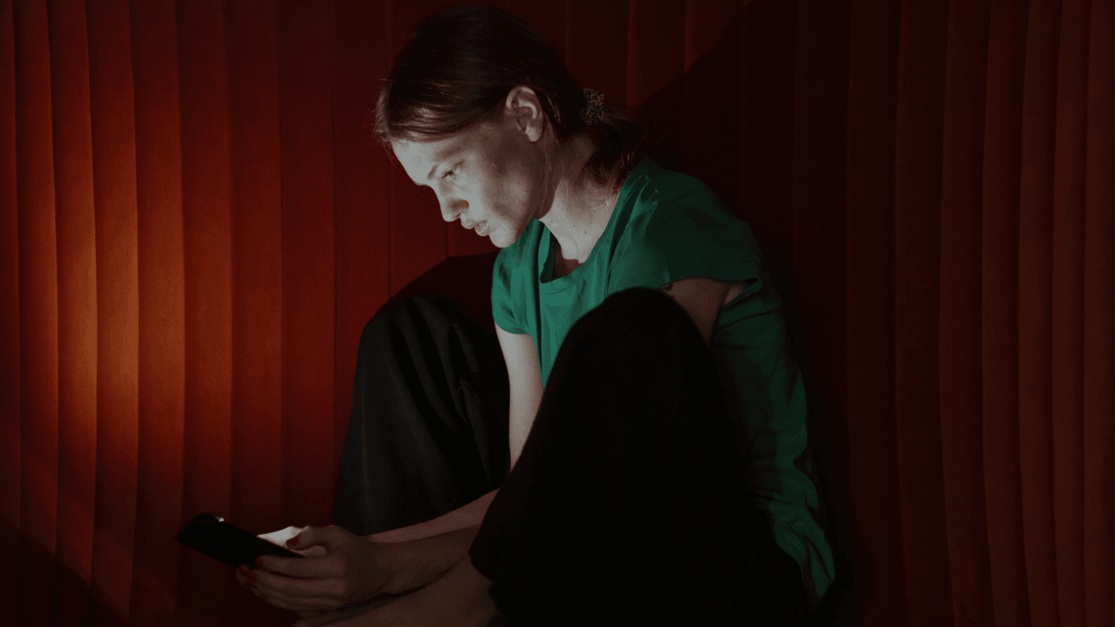 Teenager wearing green t-shirt looking at her phone in dark room