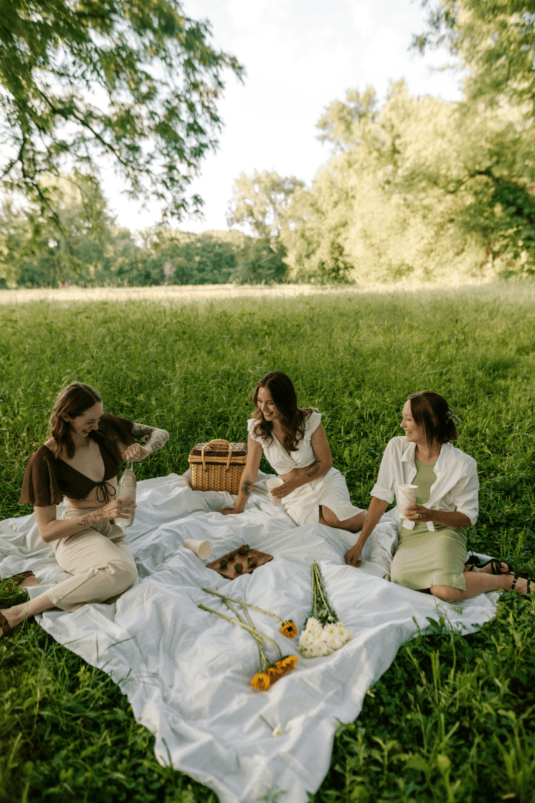 Three women sitting on white rug having picnic in park