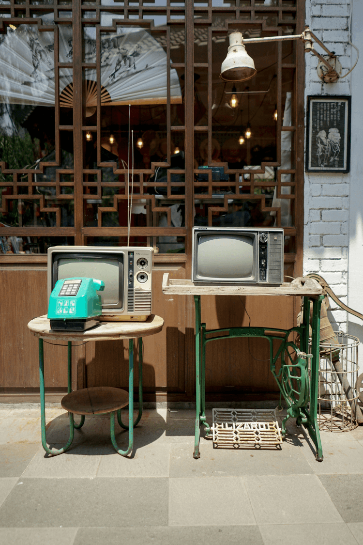 Two old televisions on tables outside a cafe