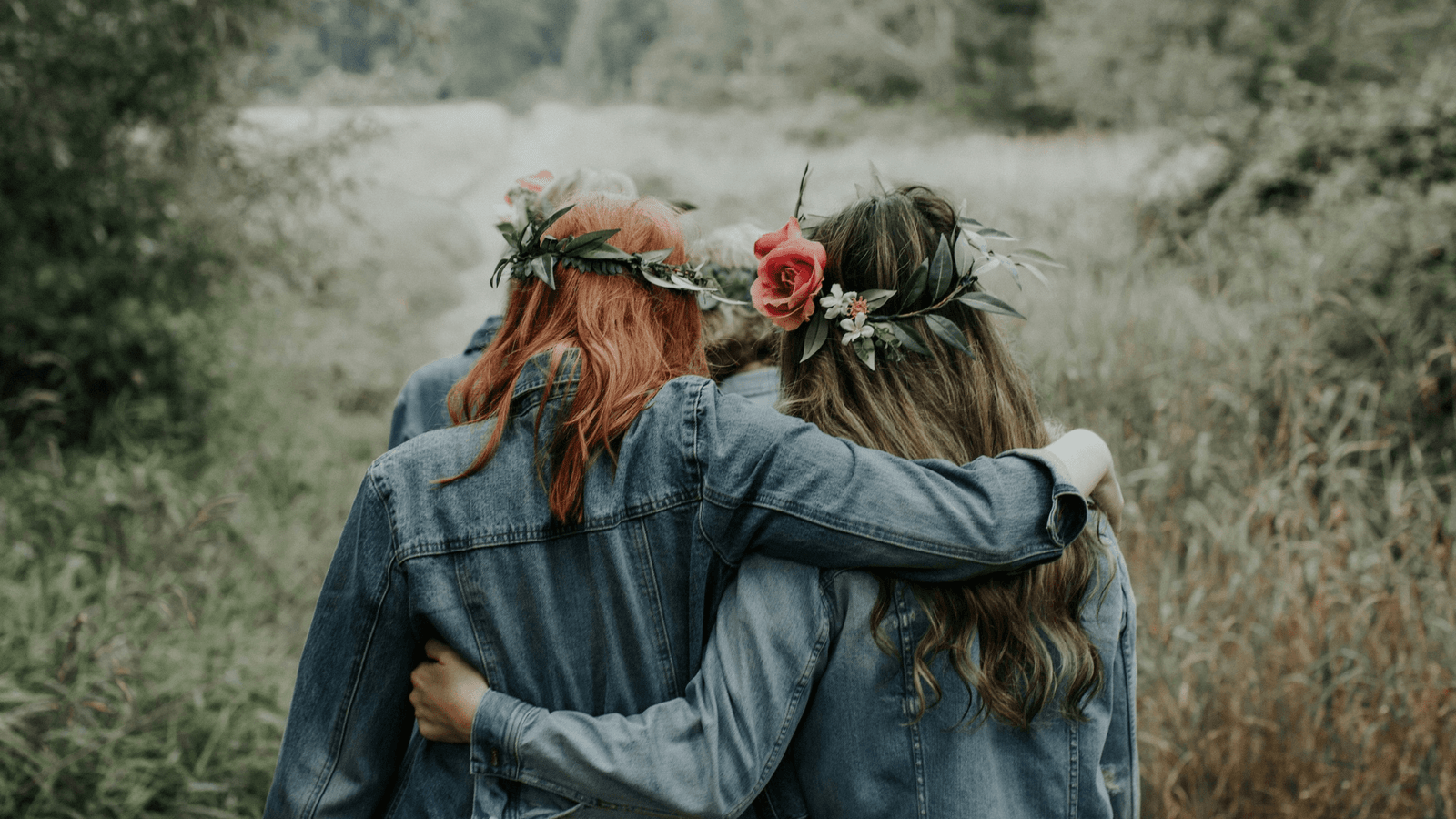 Two women with arms around waist wearing flowers in hair and denim jackets