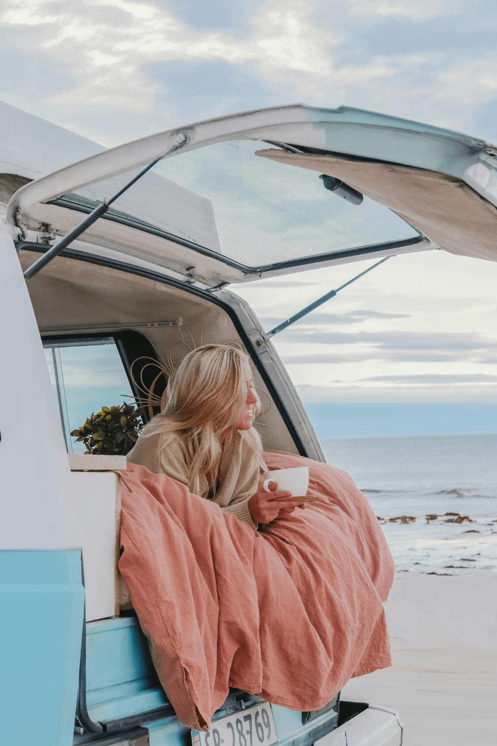 Woman having coffee in camper van next to beach