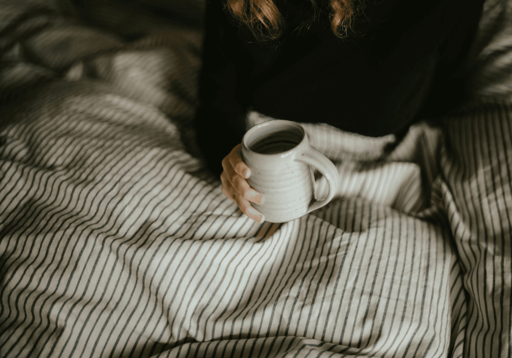 Woman holding mug un bedEmpty bed with duvet thrown back
