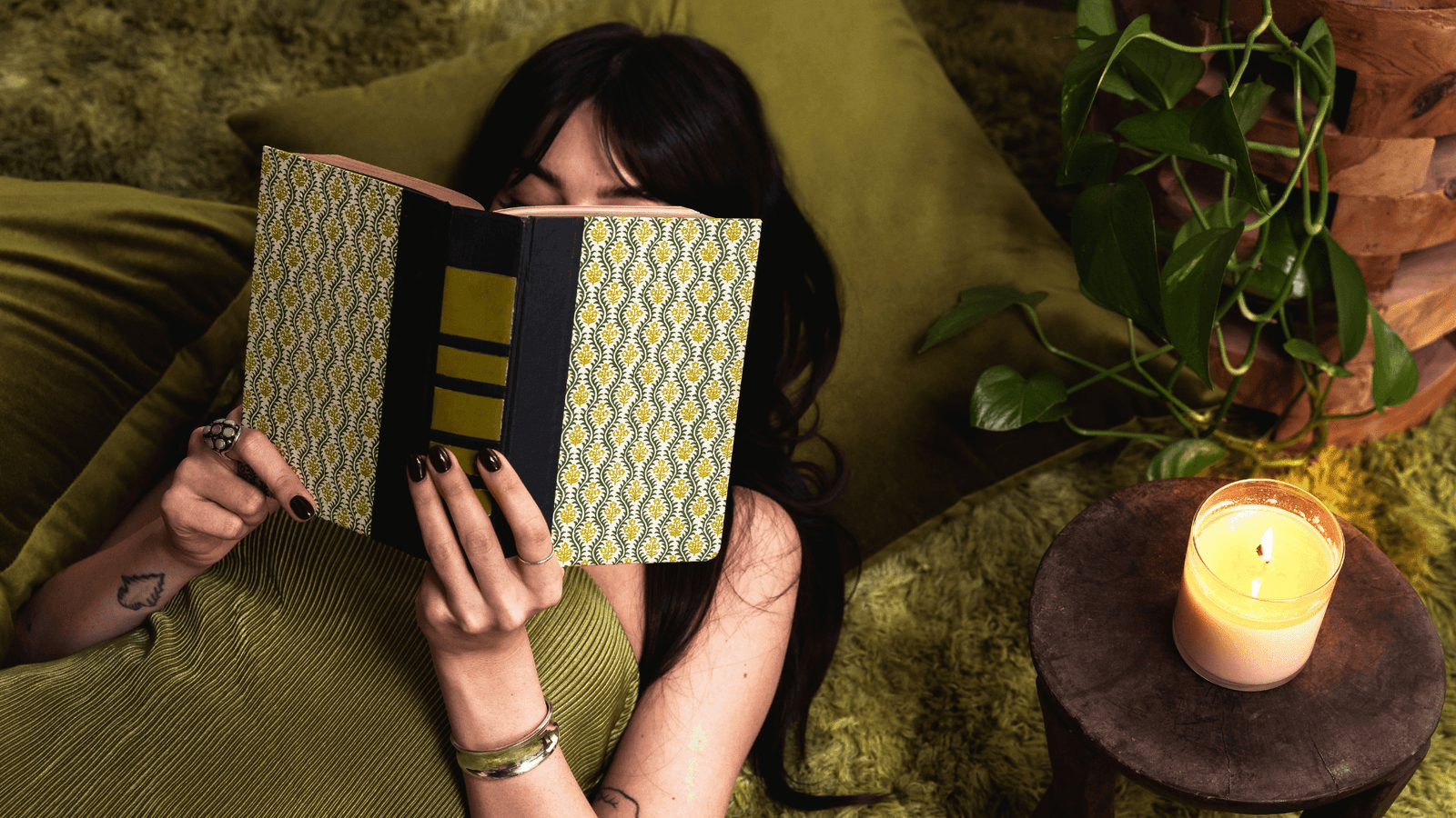 Woman lying on green cushion reading green book