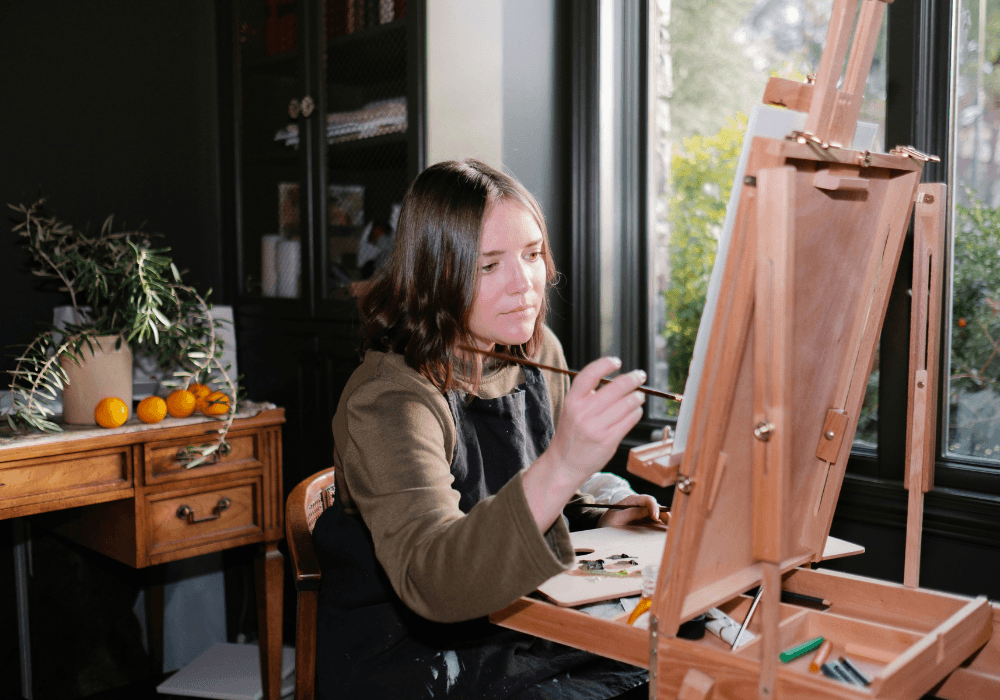 Woman painting on canvas next to window