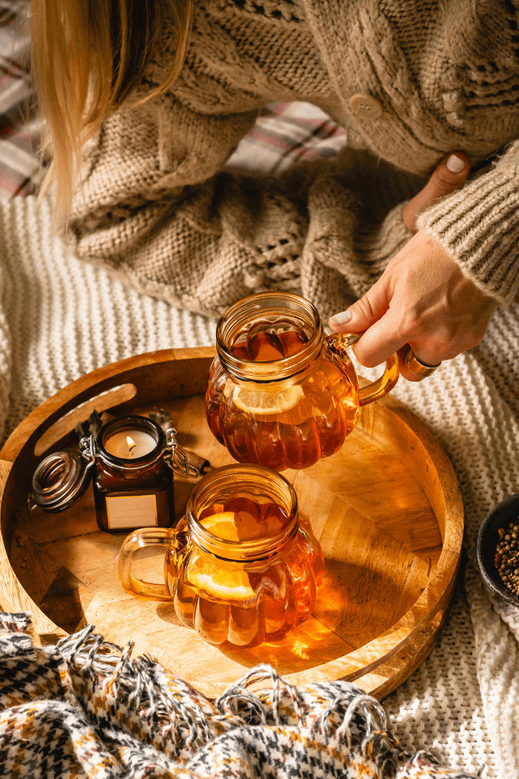 Woman putting jug of tea on tray next to candle