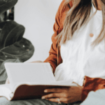 Woman wearing white t-shirt and orange cardigan reading a book