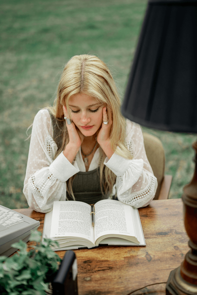 Woman reading book outside sitting at wooden table
