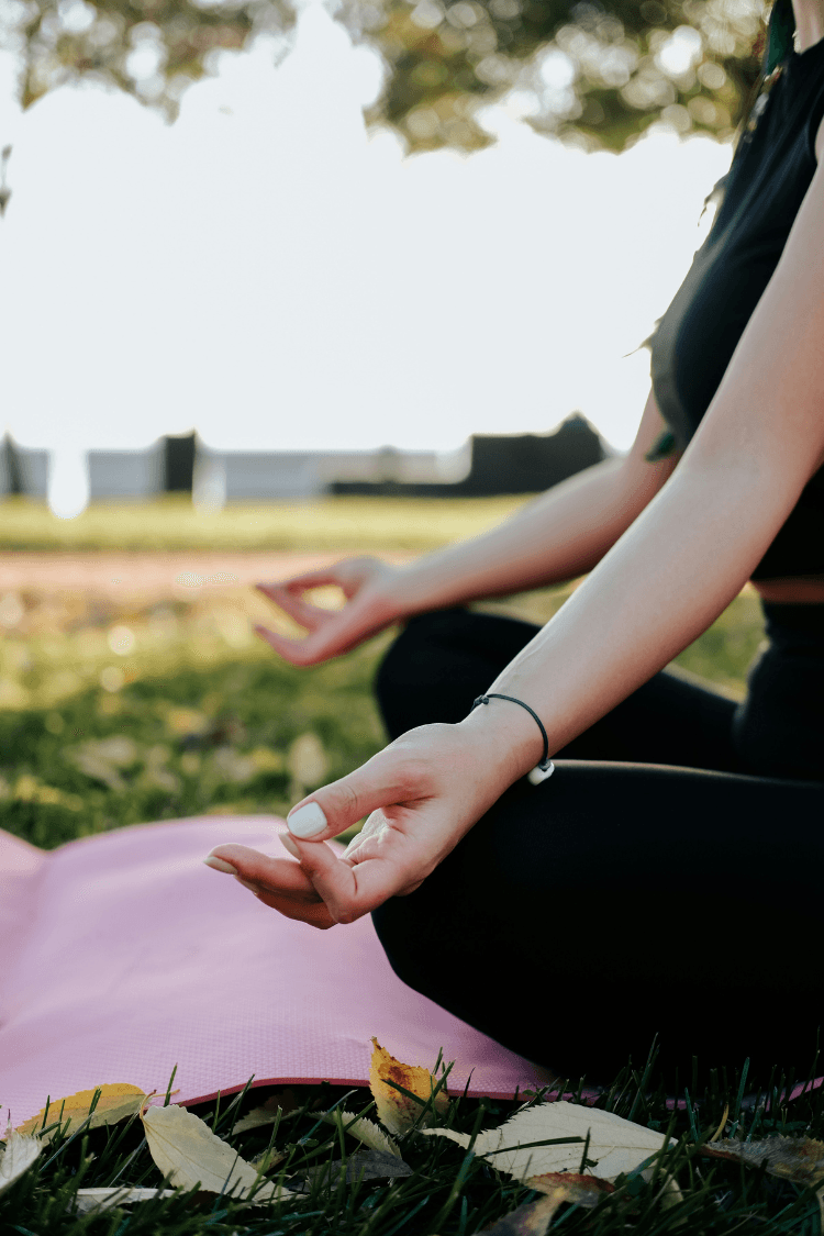 Woman sitting on pink mat in park doing a yoga pose