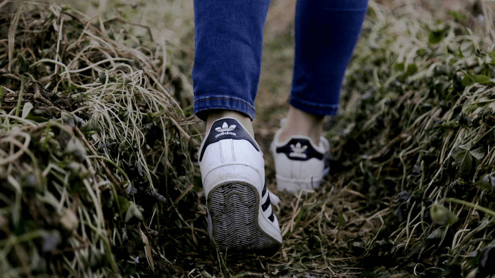 Woman walking in field wearing white Adidas trainers