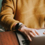 Woman wearing orange jumper typing on laptop