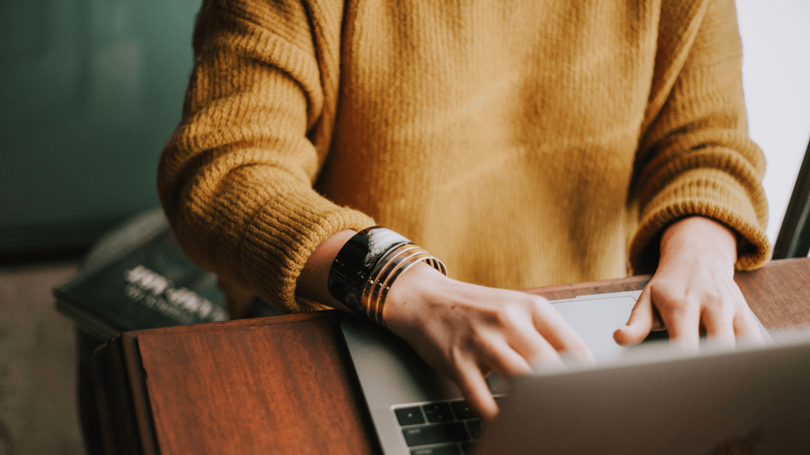Woman wearing orange jumper typing on laptop