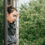 Woman wearing pyjamas looking out of the window feeling tired