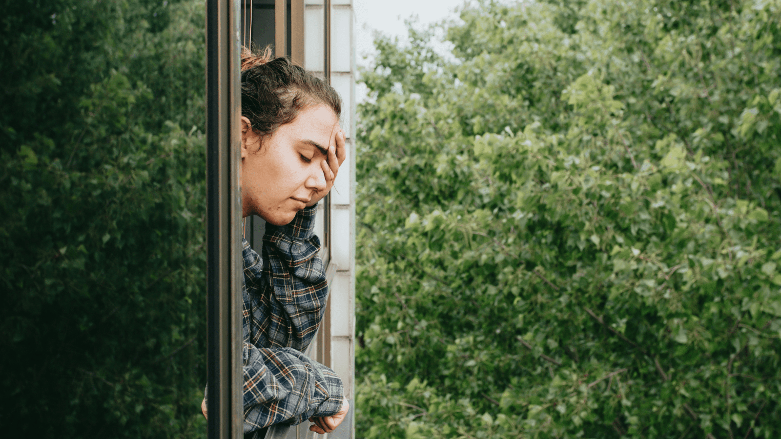 Woman wearing pyjamas looking out of the window feeling tired