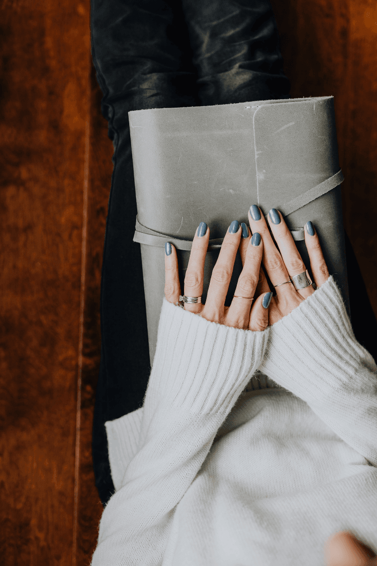 Woman with blue painted nails holding journal with grey cover