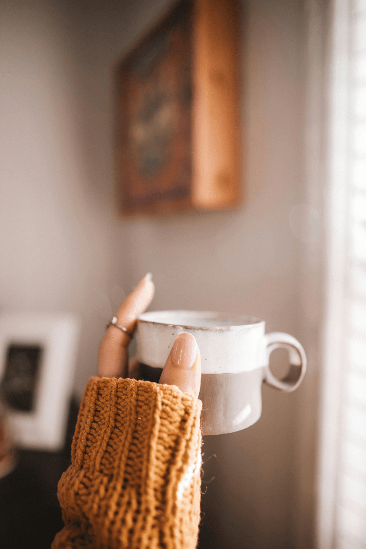 Woman's hand holding small brown and cream ceramic mug