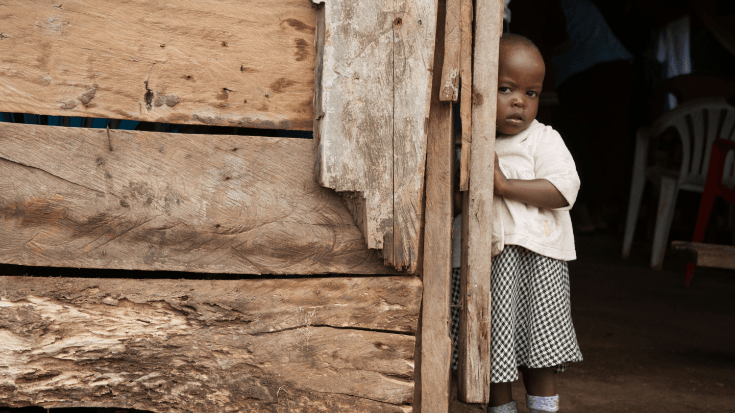 Young girl peeking out of the doorway of her home in Uganda