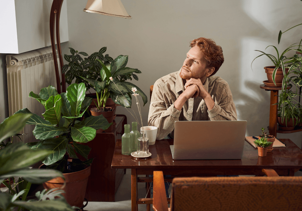 Man sitting at desk surrounded by plants thinking