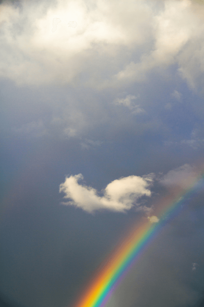 Small rainbow in dark sky below cloud