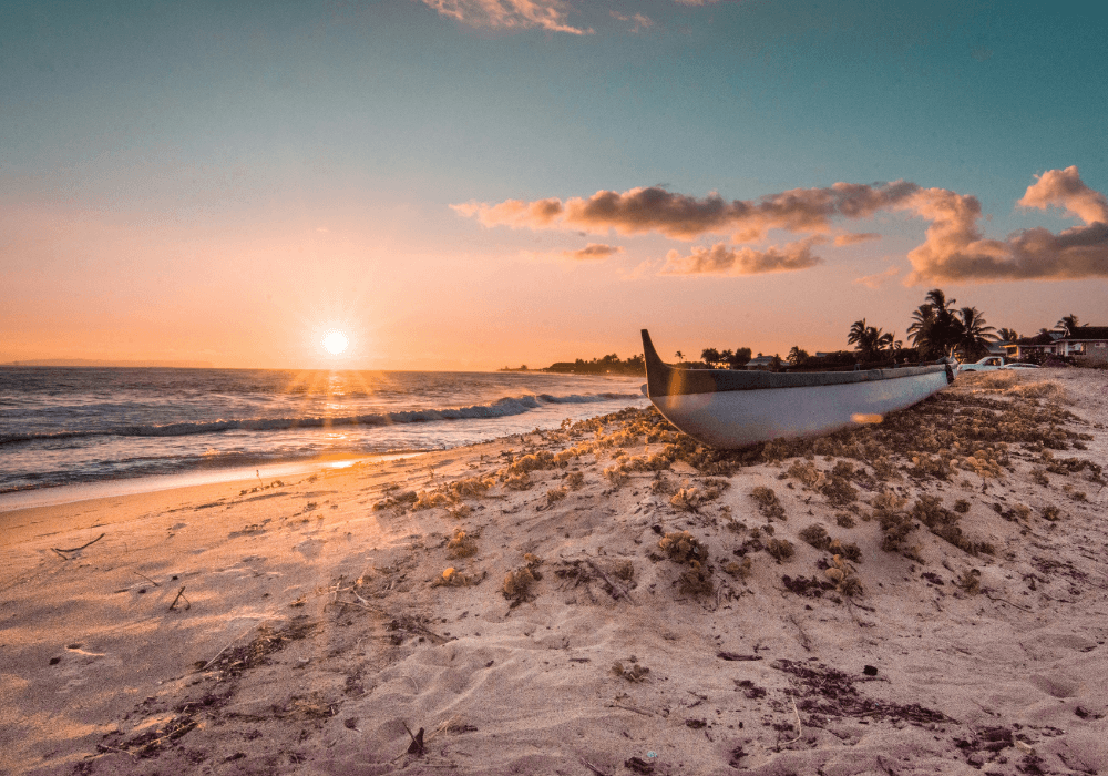 Sun setting over the sea with sand and boat in foreground
