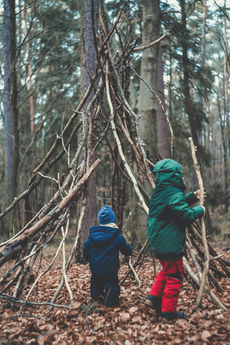 Two children building a den in the woods in autumn