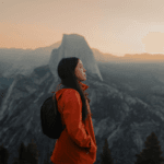 Woman in an orange jacket by a mountain range