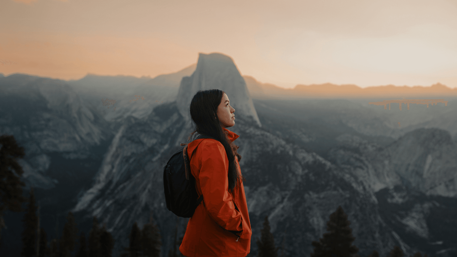 Woman in an orange jacket by a mountain range