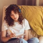 Woman with headphones on writing in notebook