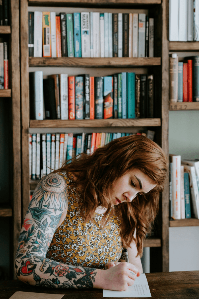 Woman writing in notebook in front of bookcase