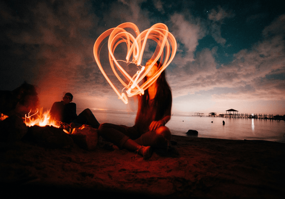 Girl on a beach making a heart shape out of fire